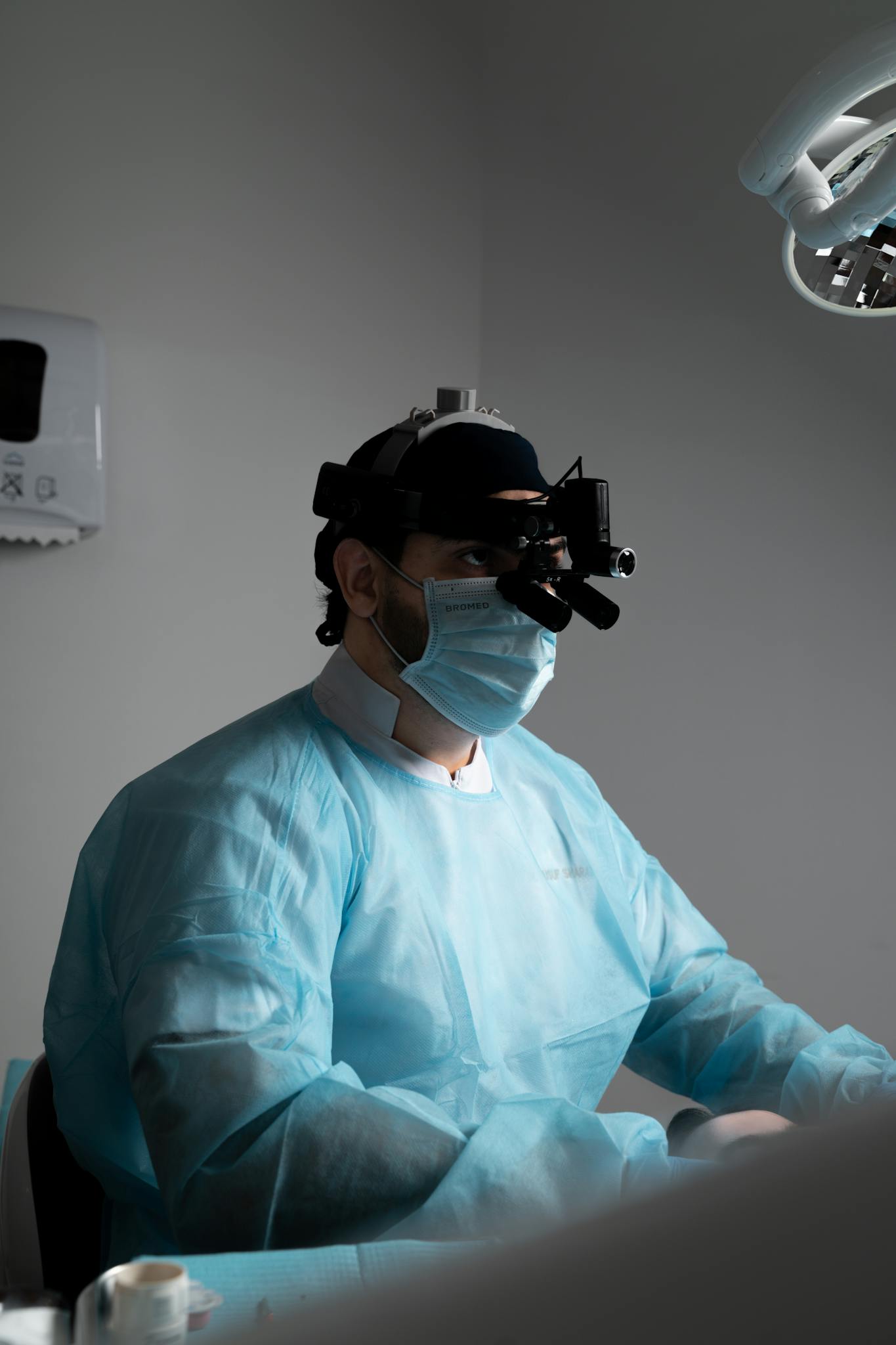A dental professional in surgical attire using magnifying eyewear for precision work.